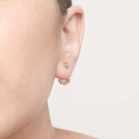 A single tiny champagne diamond center stone earrings with a halo of champagne diamond set in yellow gold on a light complexion ear. 2