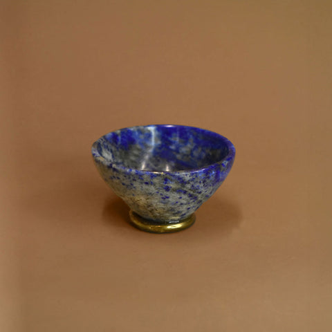 Blue lapis bowl on a bronze base against a beige background