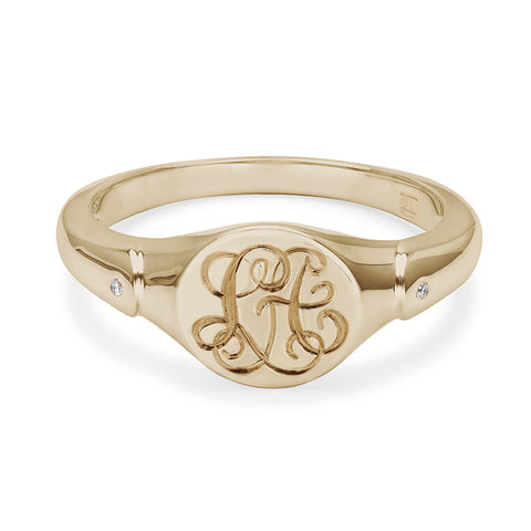 A solid gold signet ring with two white diamond accent stones with interlocking engraving in the center set in yellow gold.
