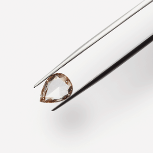 A pair of tweezers delicately holds a rose-cut pear shaped champagne diamond
