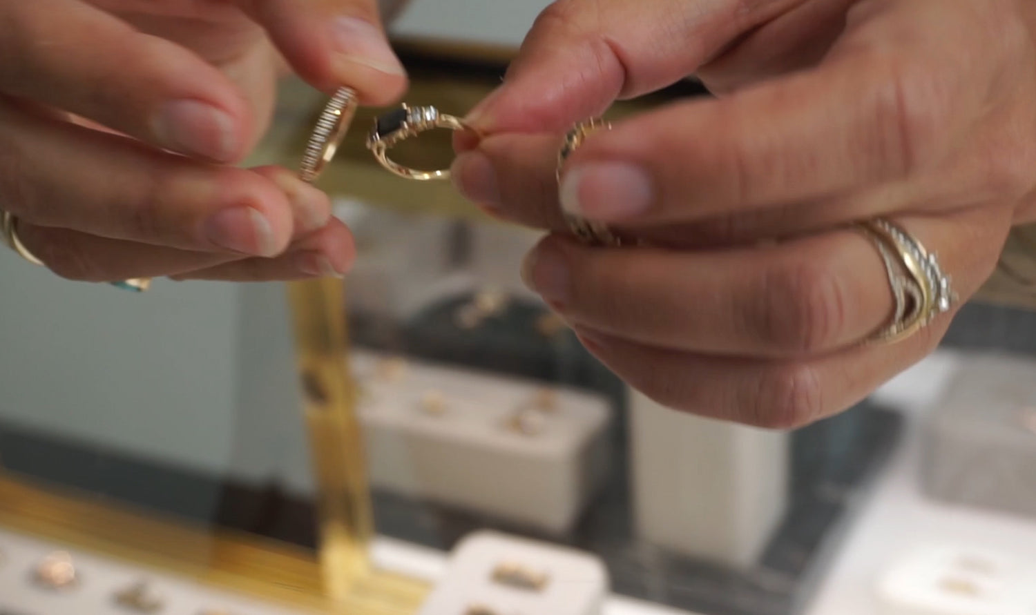 Two hands holding a five stone black diamond ring and a straight white diamond band over a jewelry case.