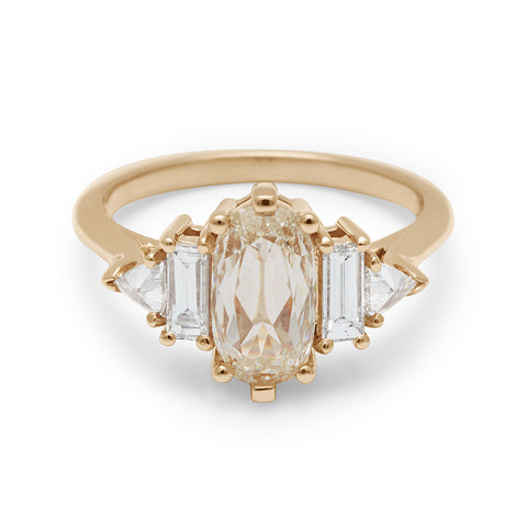 A ring with a lozenge shaped champagne diamond center stone with one baguette white diamond and one white diamond trillion on either side set in yellow gold.