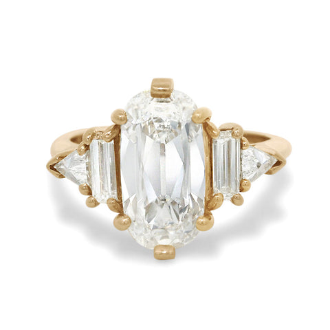 Gold five stone ring with a large elongated cushion diamond center stone and smaller baguette and trillion diamond side stones on a white background