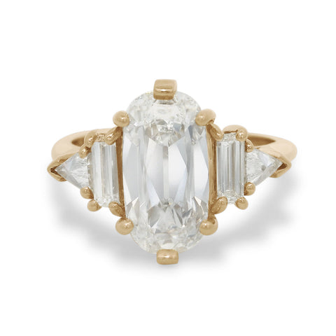 Gold five stone ring with a large elongated cushion diamond center stone and smaller baguette and trillion diamond side stones on a white background