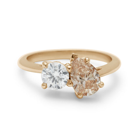 A two diamond ring with a pear champagne diamond set next to a round white diamond set in yellow gold.