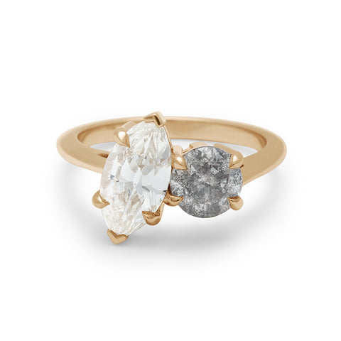 A two diamond ring with a marquise white diamond set next to a round grey diamond set in yellow gold.