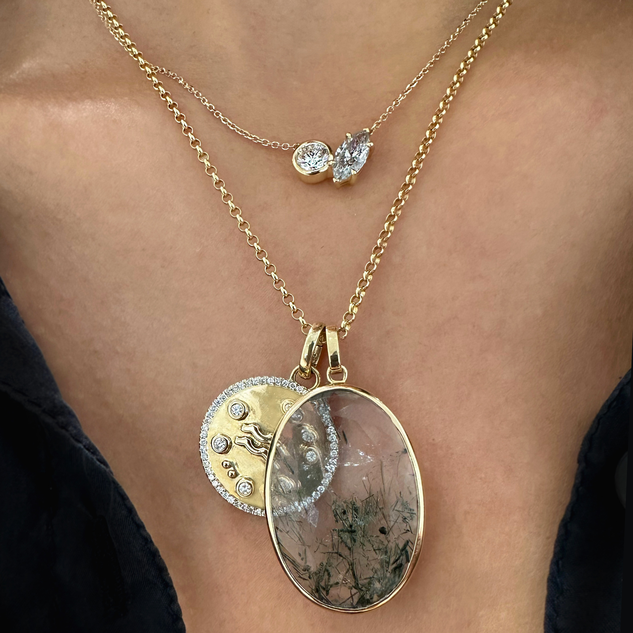 A woman wearing two different yellow gold necklaces, the shorter one with a white diamond and grey diamond and the longer one with a green gemstone and a yellow gold aquarius zodiac medallion 