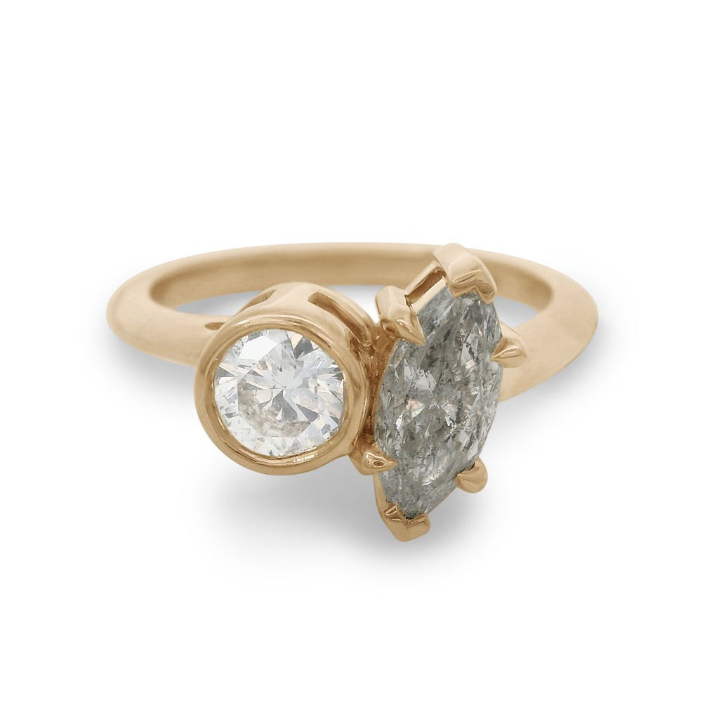 A yellow gold toi et moi engagement ring featuring a white round diamond and a grey marquise diamond on a white background