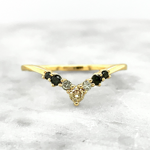 A v-shaped wedding band featuring round diamonds of different colors and shapes, including one largest champagne diamond in the center followed by small grey diamonds and finally followed by two black diamonds on either side, set in yellow gold. 
