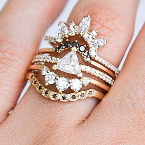 A ring stack featuring a white triangle diamond solitaire ring and nesting bands featuring an array of white and black diamonds. All set in yellow gold. 