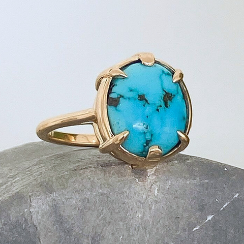 A turquoise solitaire ring featuring an oval cabochon turquoise set in yellow gold. 