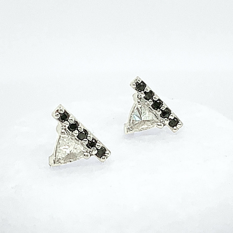 A pair of stud earrings which feature a white trillion diamond and 5 1mm round black diamonds set in white gold in the silhouette of a triangle. 