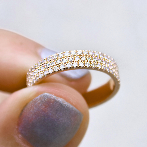 A three row white diamond (1mm size) flat band set in yellow gold held between two fingers. 