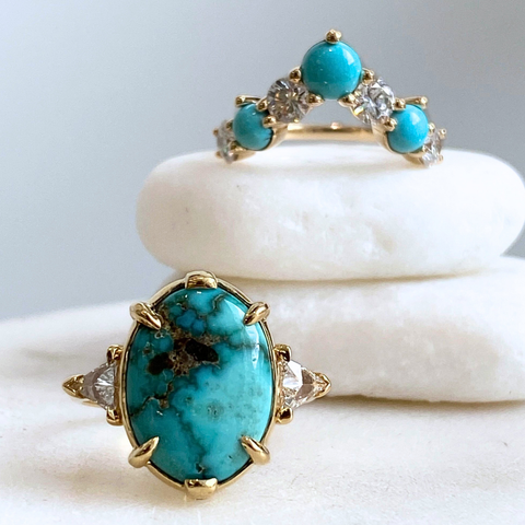 One three stone turquoise ring featuring an oval cabochon turquoise and white trillion diamond side stones set in yellow gold as well as a turquoise and white diamond curved wedding band set in yellow gold. 
