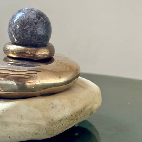 A bronze and porcelain stone object featuring a grey agate gemstone sphere on a glass table