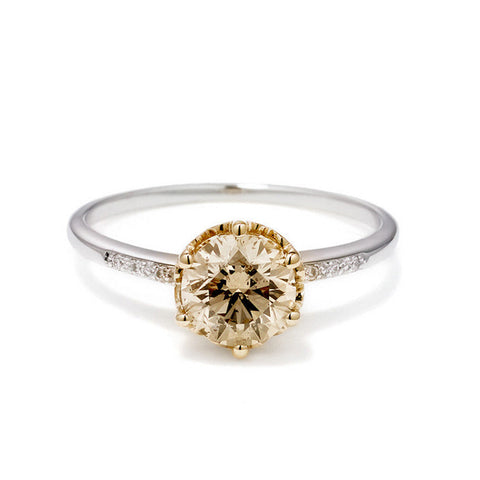 A solitaire ring with a round shaped champagne diamond with white diamond pave on either side set in a yellow gold basket and a white gold band.