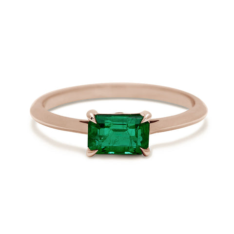 An east/west solitaire ring with an emerald shape green emerald stone set in rose gold.