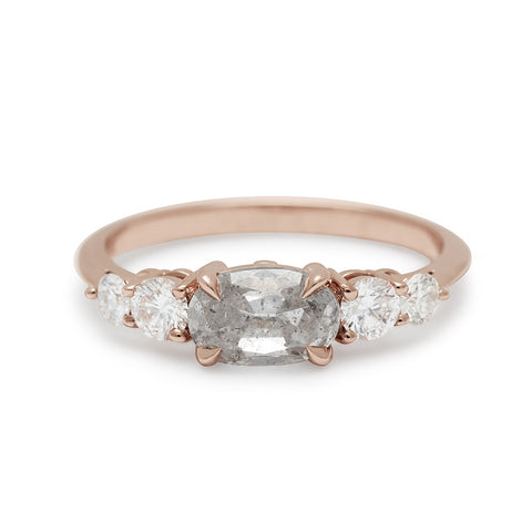 A ring with an oval shaped grey diamond center stone with two round white diamonds on either side set in rose gold.