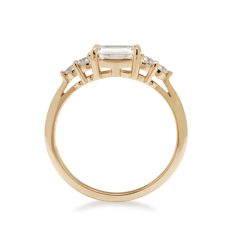 A side view of a ring with an emerald cut and shaped white diamond center stone with two round white diamonds on either side set in yellow gold., Yellow Gold 4