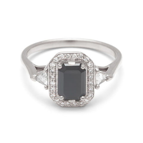 A three stone engagement ring with an emerald cut and emerald shape black diamond center stone surrounded by a white diamond pave halo with two white diamond trillion side stones set in white gold., White Gold 4