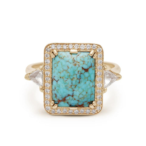 A one of a kind three stone engagement ring with an emerald shape turquoise center stone surrounded by a white diamond pave halo with two white diamond trillion side stones set in yellow gold.