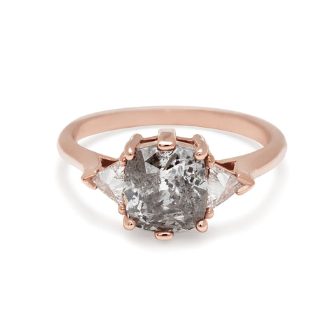 A three stone engagement ring with an cushion cut grey diamond center stone with two white diamond trillion side stones set in rose gold.