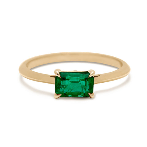 An east/west solitaire ring with an emerald shape green emerald center stone set in yellow gold.