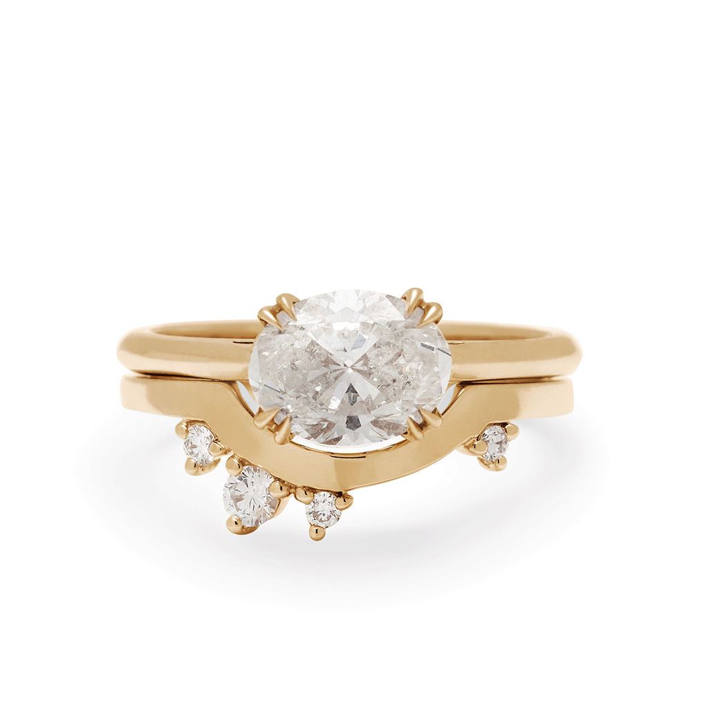 An east/west solitaire ring with an oval shape white diamond stone set in yellow gold above a asymmetrical white diamond curve band.