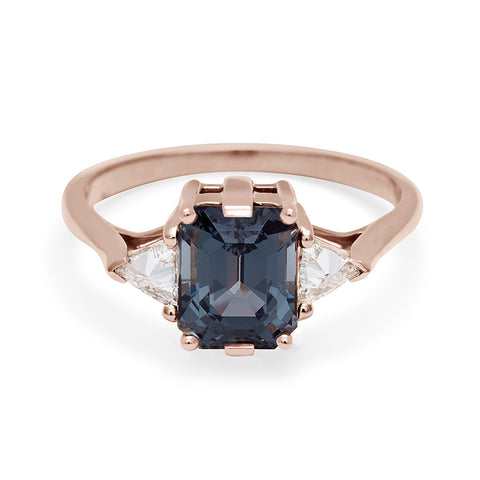 A three stone engagement ring with an emerald cut and emerald shape grey spinel center stone with two white diamond trillion side stones set in rose gold., Rose Gold 4