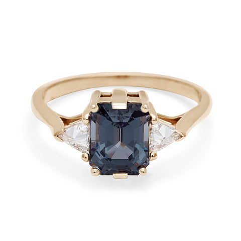 A three stone engagement ring with an emerald cut and emerald shape grey spinel center stone with two white diamond trillion side stones set in yellow gold., Yellow Gold