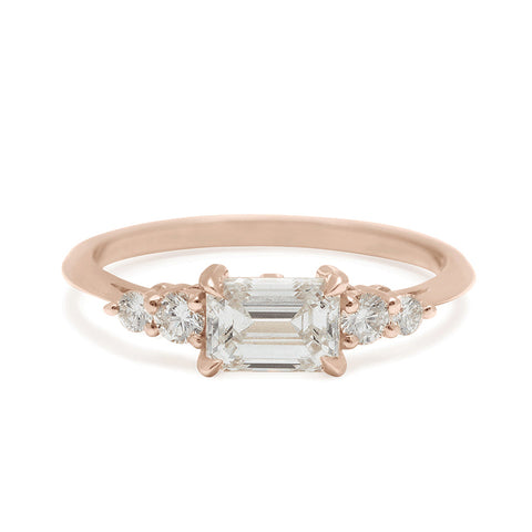 A ring with an emerald cut and shaped white diamond center stone with two round white diamonds on either side set in rose gold., Rose Gold 5