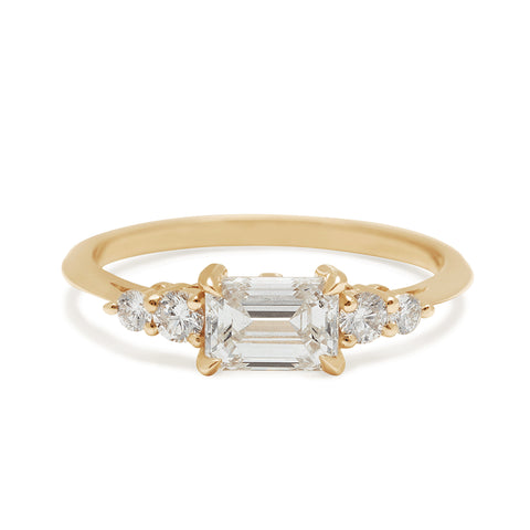 A ring with an emerald cut and shaped white diamond center stone with two round white diamonds on either side set in yellow gold., Yellow Gold