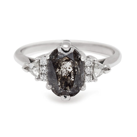 An oval shape grey diamond center stone ring with three round white diamonds on either and two white diamond trillions on the outer edges of each side set in white gold.