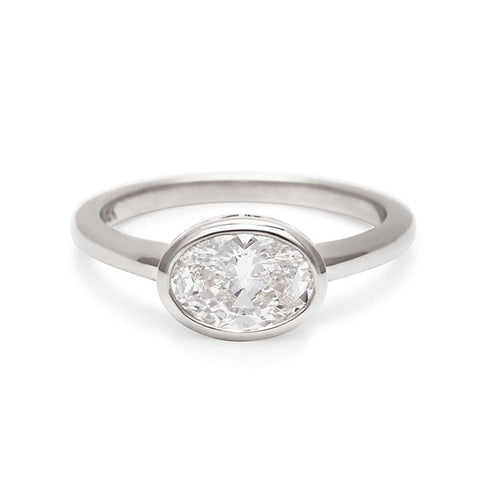 A east west oval shaped brilliant cut bezel set white diamond set in white gold.