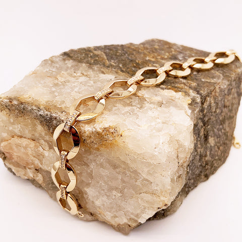 A large chain bracelet with white diamond accents set in yellow gold on a stone.