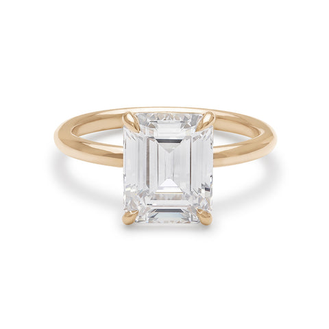 An emerald cut and shaped white diamond solitaire engagement ring with a hidden white diamond pave halo under the center stone set in yellow gold.