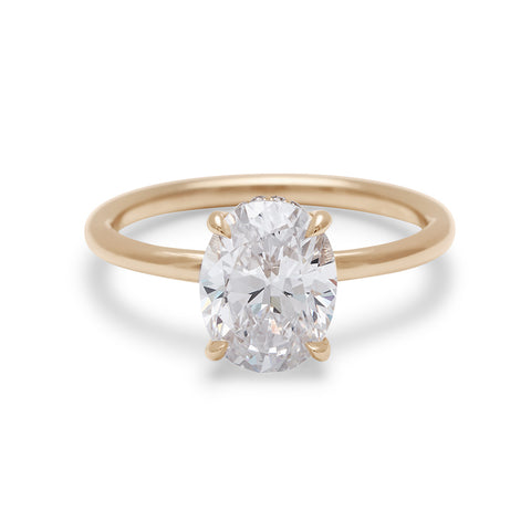 An oval shaped white diamond solitaire engagement ring with a hidden white diamond pave halo under the center stone set in yellow gold.