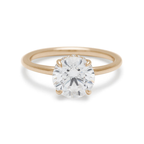 A round shaped white diamond solitaire engagement ring with a hidden white diamond pave halo under the center stone set in yellow gold.