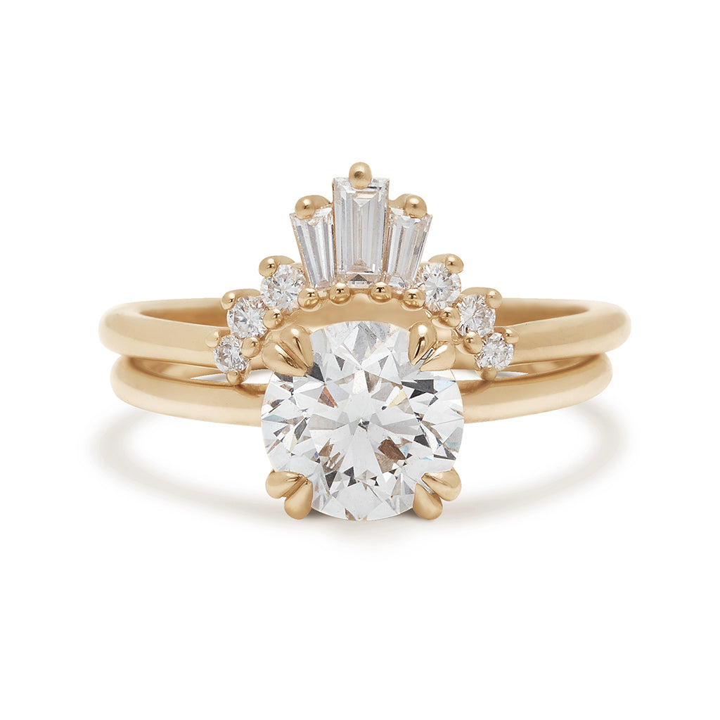 A solitaire round white diamond ring with double claw prongs set in yellow gold above a triple baguette white diamond band in yellow gold.