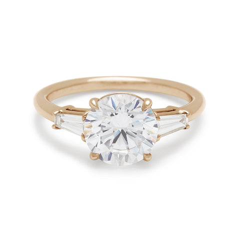 A three stone engagement ring with a round white diamond center stone and two white diamond tapered baguettes on either side set in 14k gold.