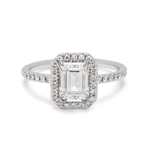 An engagement ring with an emerald cut white diamond center stone surrounded by a white diamond pave halo set in white gold.