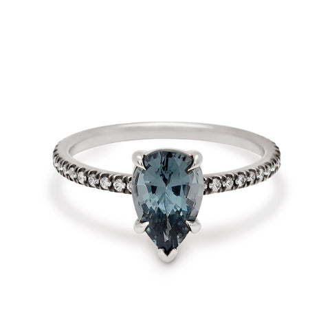 A solitaire pear shaped grey spinel ring with claw prongs with white diamond pave on the band set in black rhodium and white gold.