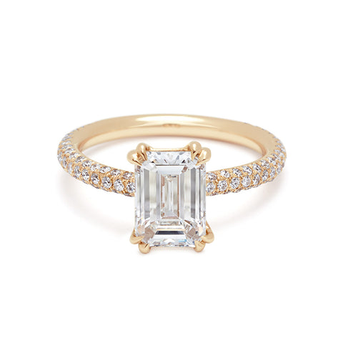 A solitaire emerald shape and emerald cut white diamond ring with double claw prongs with three rows of white diamond pave on the band set in yellow gold.