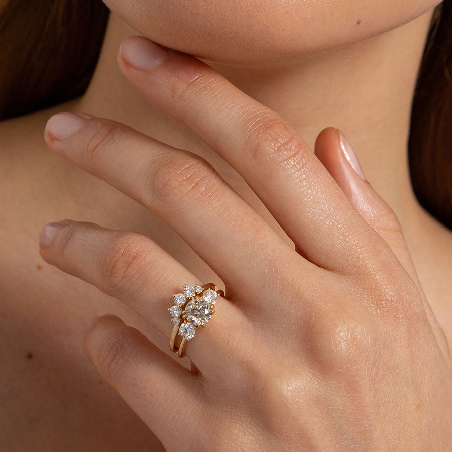 A curved 5 white diamond band set in yellow gold above a three stone ring with a champagne diamond center stone on a light-complexion hand. Available in Yellow Gold, Rose Gold, White Gold.