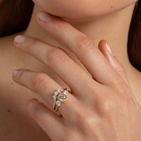 Female Hand wearing A curved 5 white diamond band set in yellow gold above a three stone ring with a champagne diamond center stone on a light-complexion hand. 3