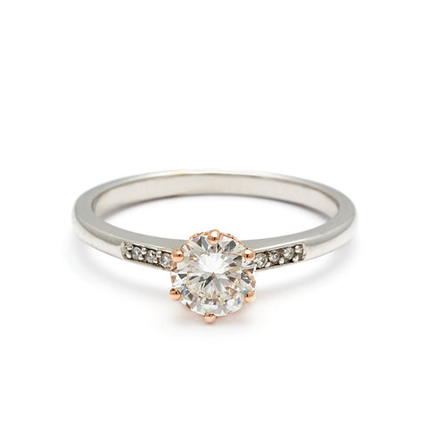 A solitaire ring with a round shape white diamond with white diamond pave on either side set in a rose gold basket and white gold band.