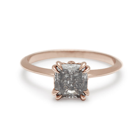 A solitaire ring with a cushion cut grey diamond with double claw prongs set in a knife edge rose gold band.