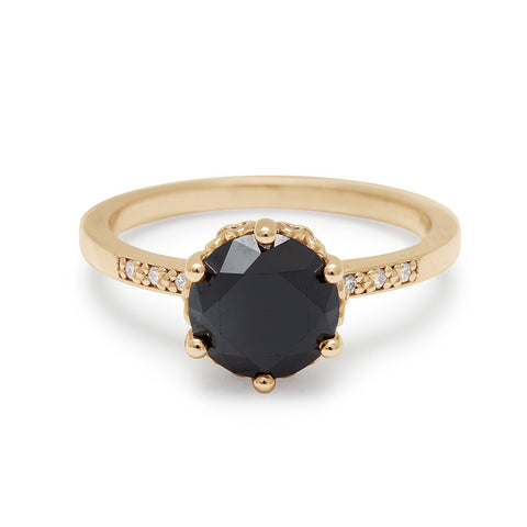 A solitaire ring with a round black diamond with white diamond pave on either side set in yellow gold.