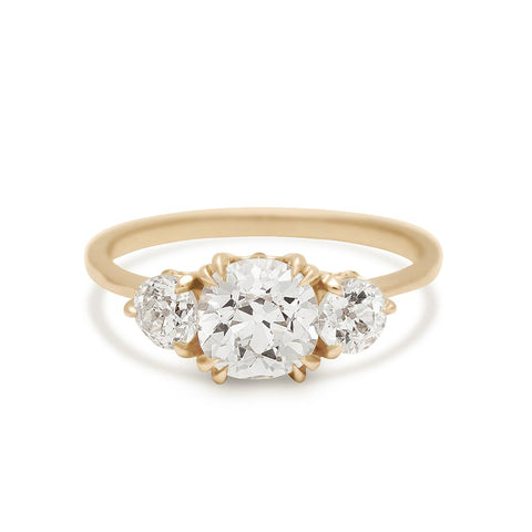 A three stone engagement ring with a round shape old mine cut white diamond center stone with two white diamond round side stones set in yellow gold.