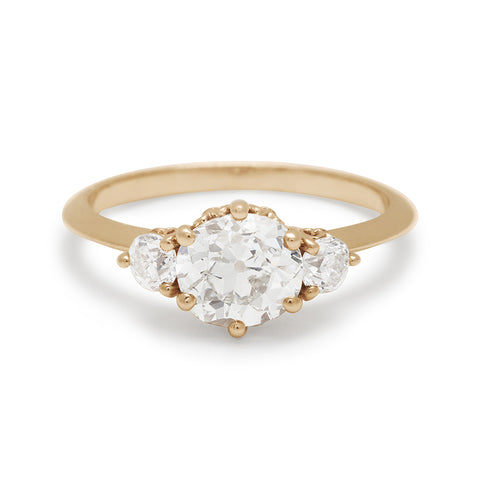 A three stone engagement ring with a round shape white diamond center stone with two white diamond round side stones set in yellow gold.